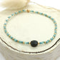 Bracelet en perles bleues et pierre noire posée sur un rond de bois écru 