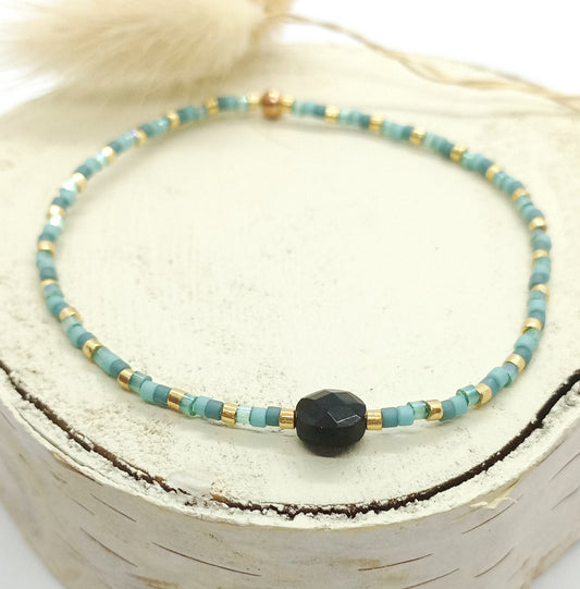 Bracelet en perles bleues et pierre noire posée sur un rond de bois écru 