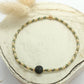 Bracelet en perles miyuki kaki et pierre onyx noire posé sur un rond de bois écru. 