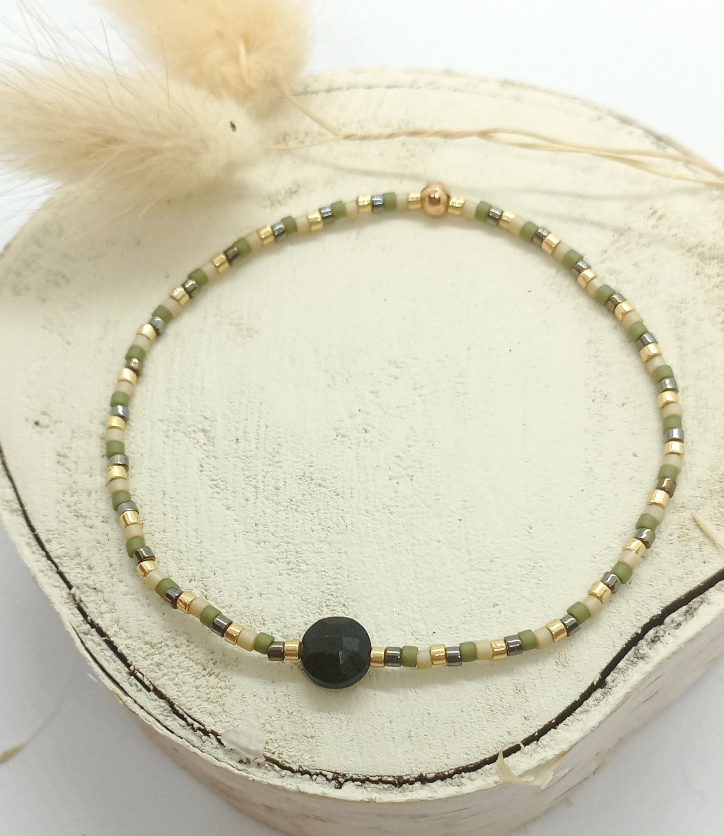 Bracelet en perles miyuki kaki et pierre onyx noire posé sur un rond de bois écru. 