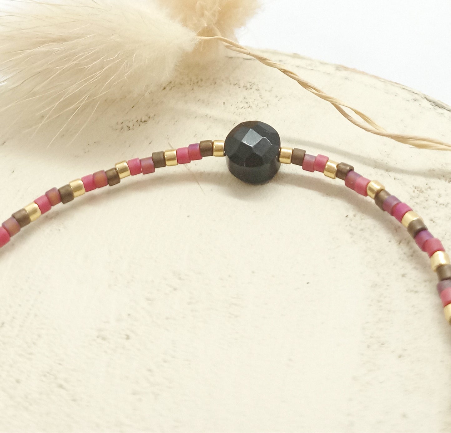 Perles Miyuki roses, marron et dorées et pierre onyx noire sur un rond de bois écru.