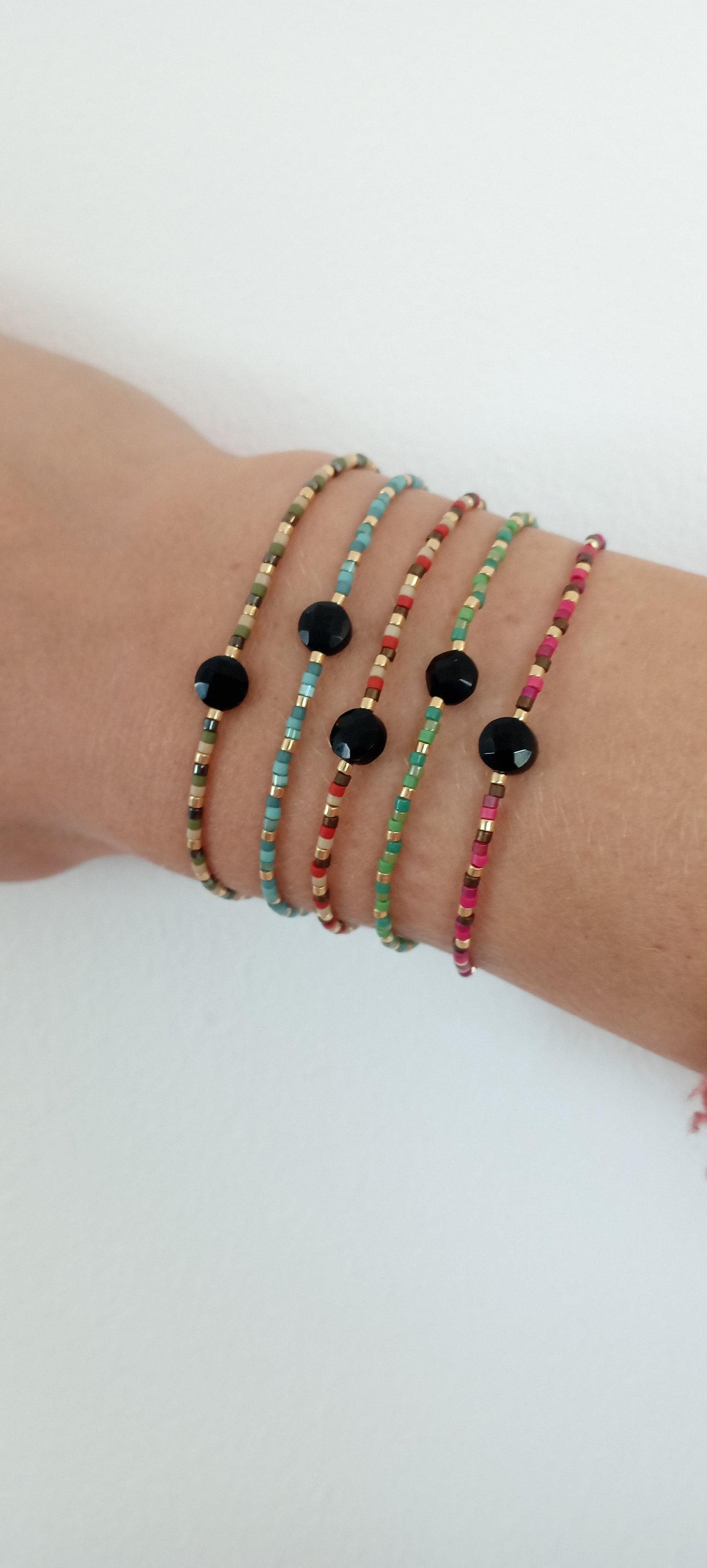 Cinq bracelets en perles miyuki colorés et pierre centrale onyx porté sur un poignet sur fond blanc.