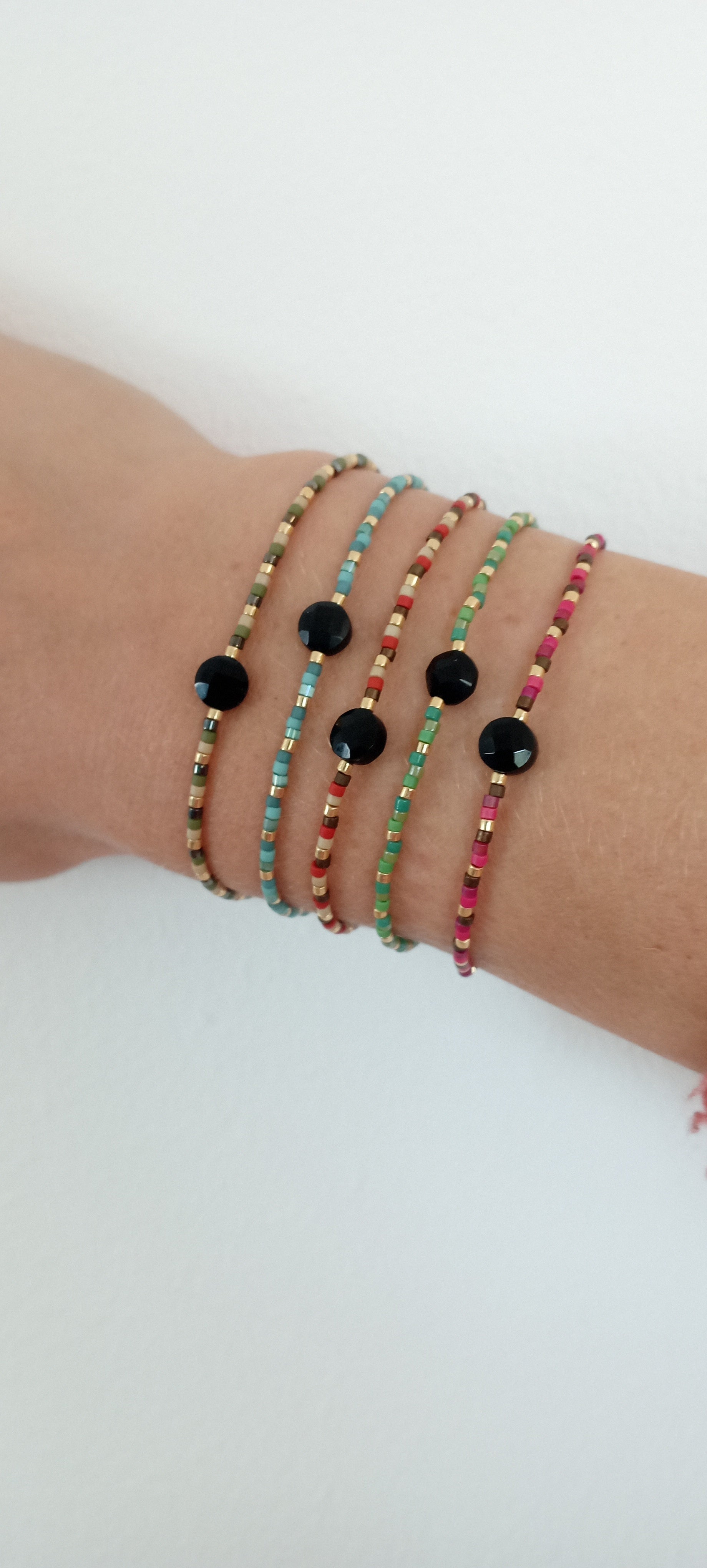 Cinq bracelets en perles miyuki colorés et pierre centrale onyx porté sur un poignet sur fond blanc. 
