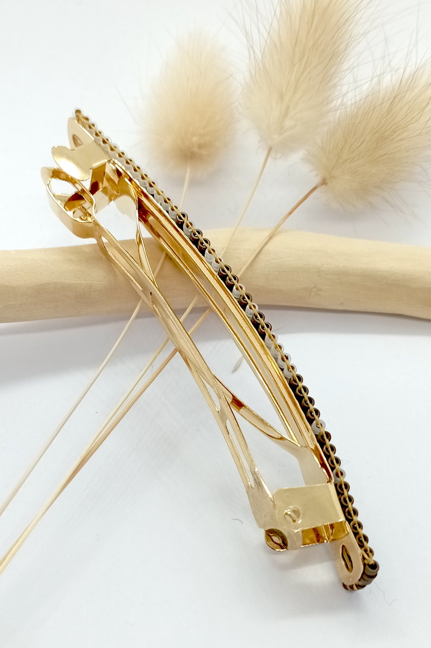 Barrette pour cheveux en métal dorée sur un fond blanc et bois clair. 