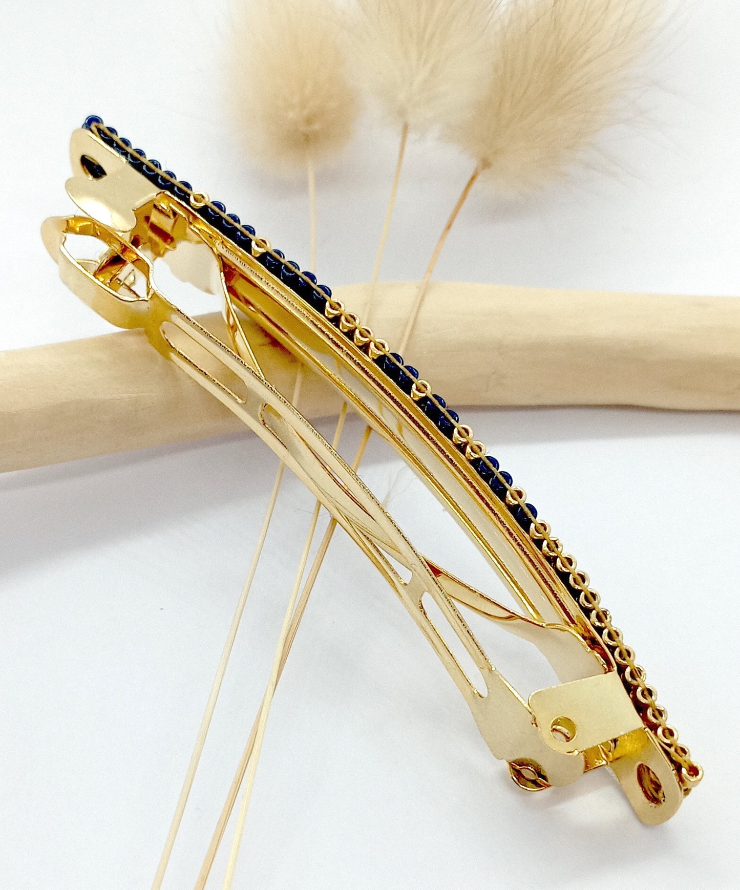 Barrette pour cheveux en métal doré sur un fond blanc et une branche de bois.