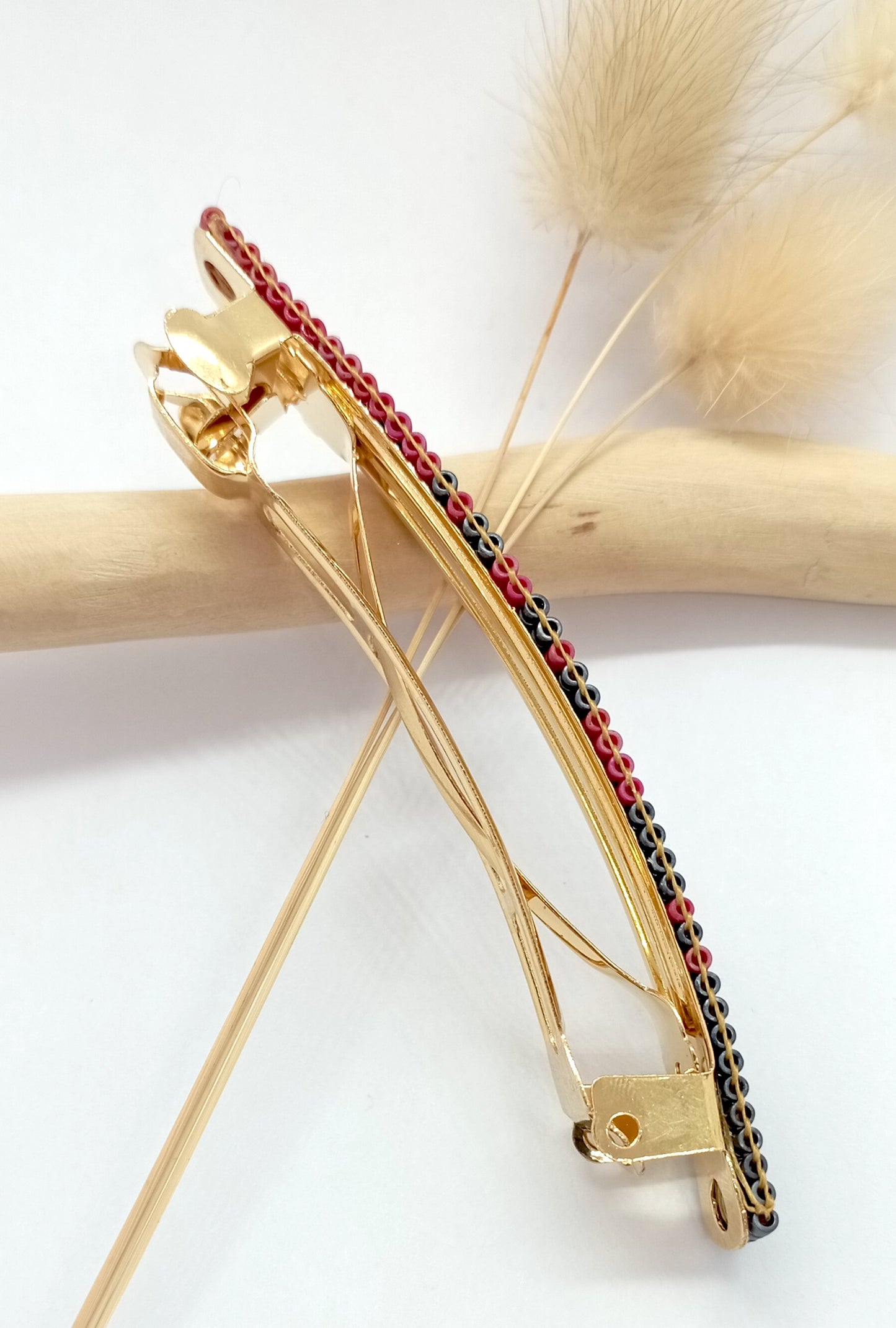 Barrette en métal dorée sur un fond blanc et une branche de bois clair.