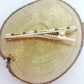Pince crocodile en métal doré avec dent, posée sur un rond de bois et un fond blanc.