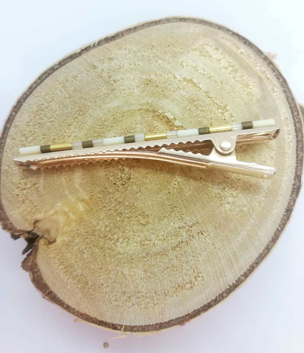 Pince crocodile en métal doré avec dent, posée sur un rond de bois et un fond blanc.