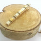 Barrette pour cheveux type pince crocodile en métal doré et perles plate, posée sur un rond de bois et un fond blanc. 
