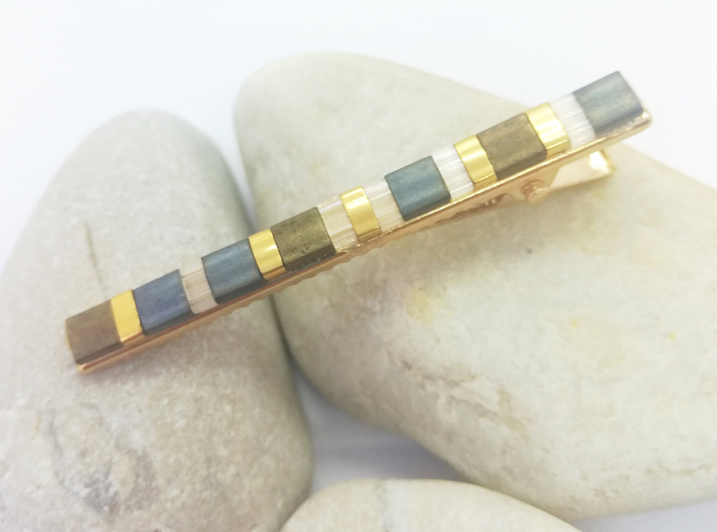 Barrette pour cheveux en perles miyuki tila posée sur des cailloux et un fond blanc.