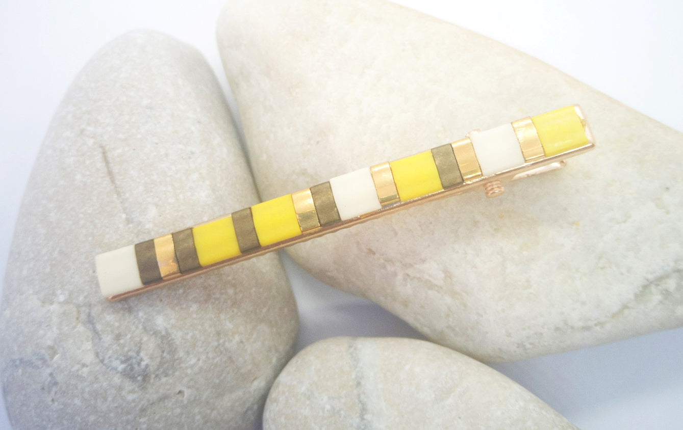 Barrette pour cheveux en perles de verres de couleur posée sur des cailloux et un fond blanc.