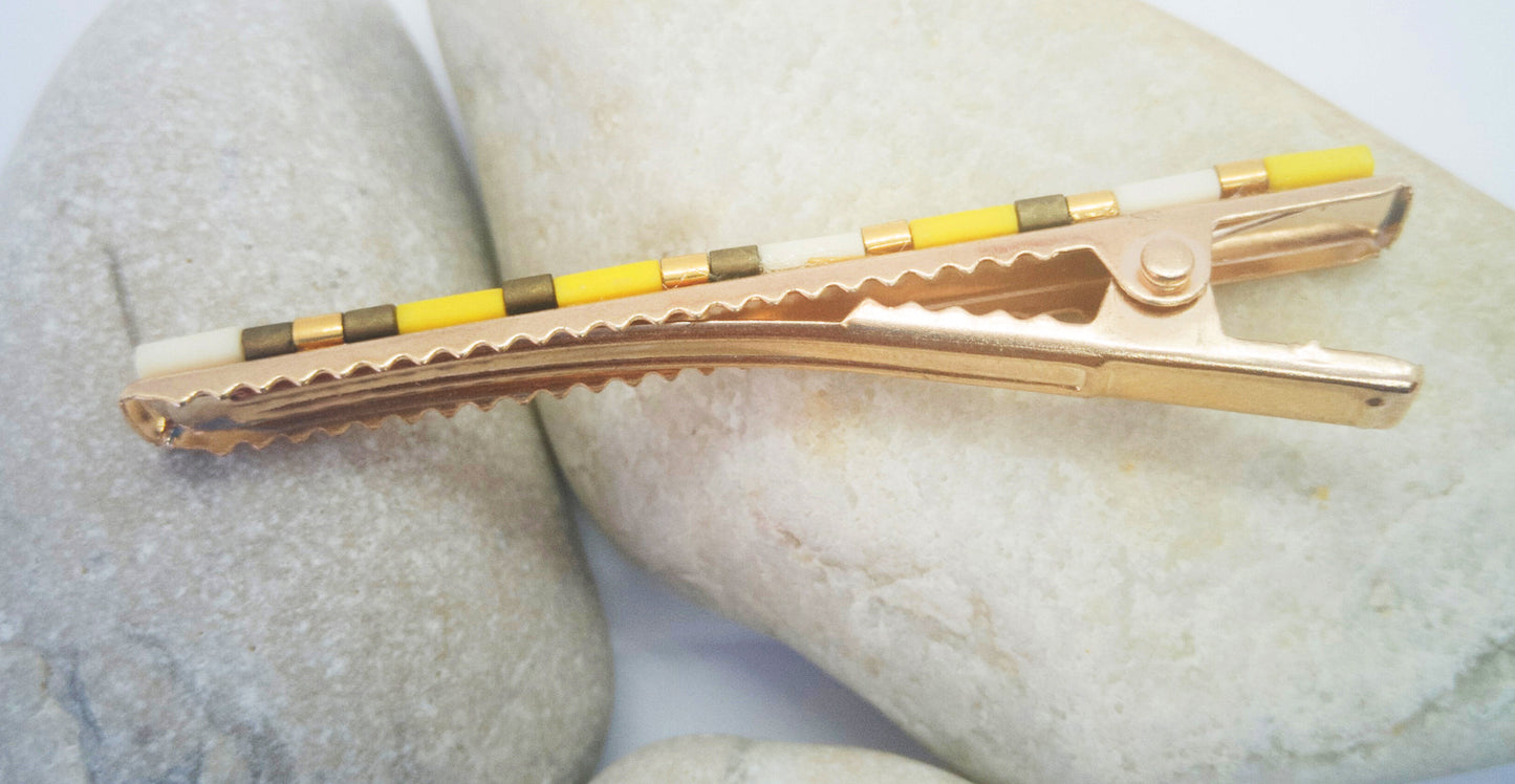 Pince crocodile en métal doré avec dents, posée sur des cailloux et un fond blanc. 