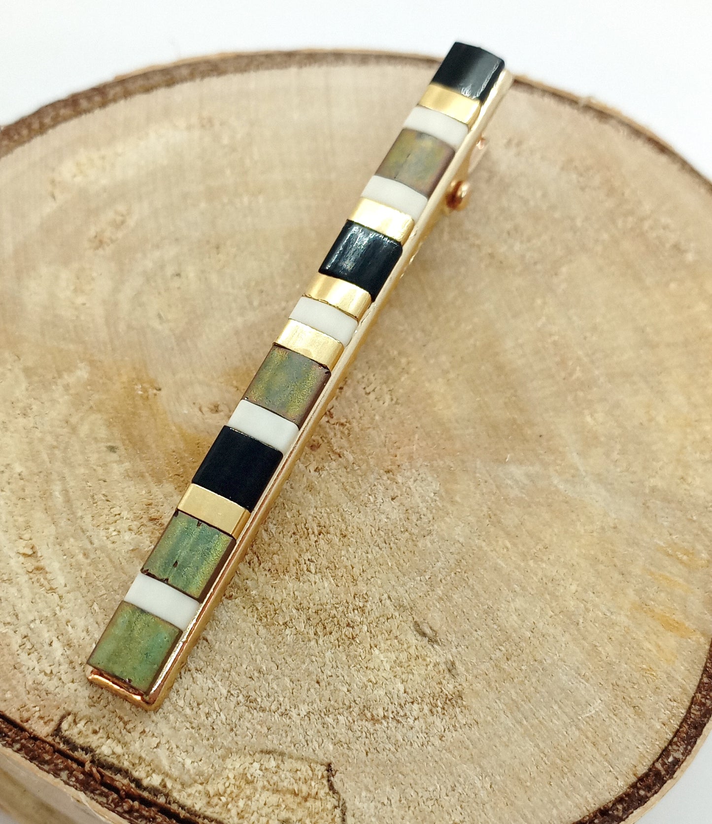 Barrette pour cheveux type pince crocodile en métal doré et perles miyuki tila, posée sur un rond de bois