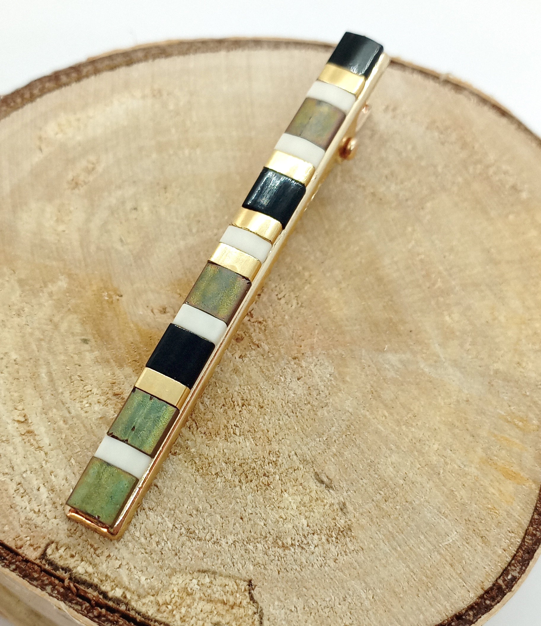 Barrette pour cheveux type pince crocodile en métal doré et perles miyuki tila, posée sur un rond de bois 