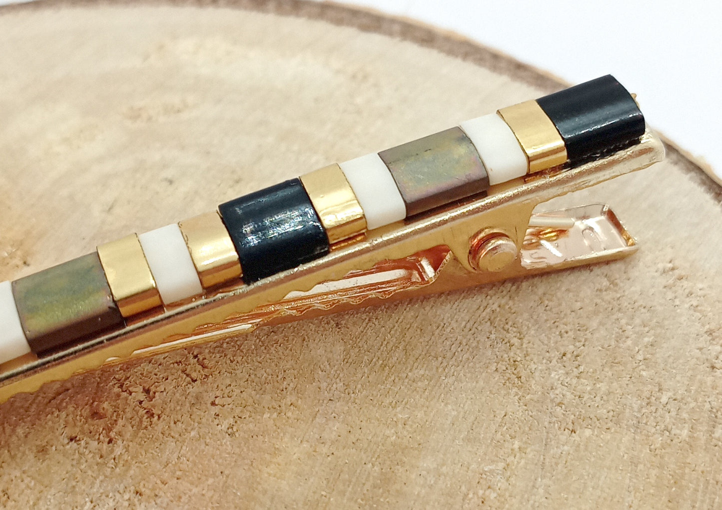 Barrette pour cheveux en métal doré et perles miyuki tila posé sur un rond de bois.