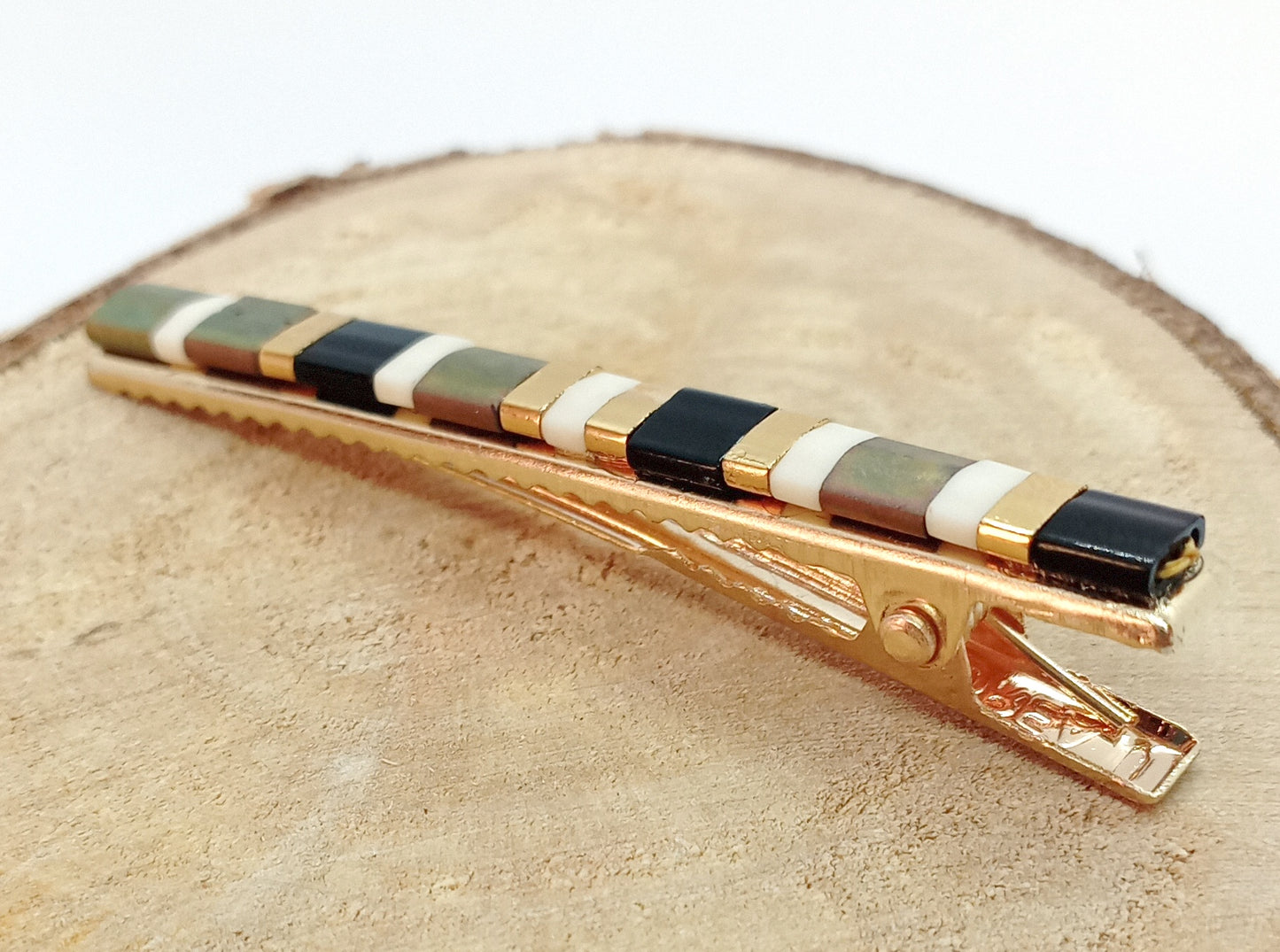 Pince crocodile pour cheveux en métal doré et perles en verre de couleur, posée sur un rond de bois.