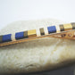 Pince crocodile en métal doré et perles plates de couleurs, posée sur des cailloux et un fond blanc