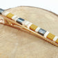 Pince crocodile en métal doré et en perles plates de couleurs posé sur un rond de bois et un fond blanc. 