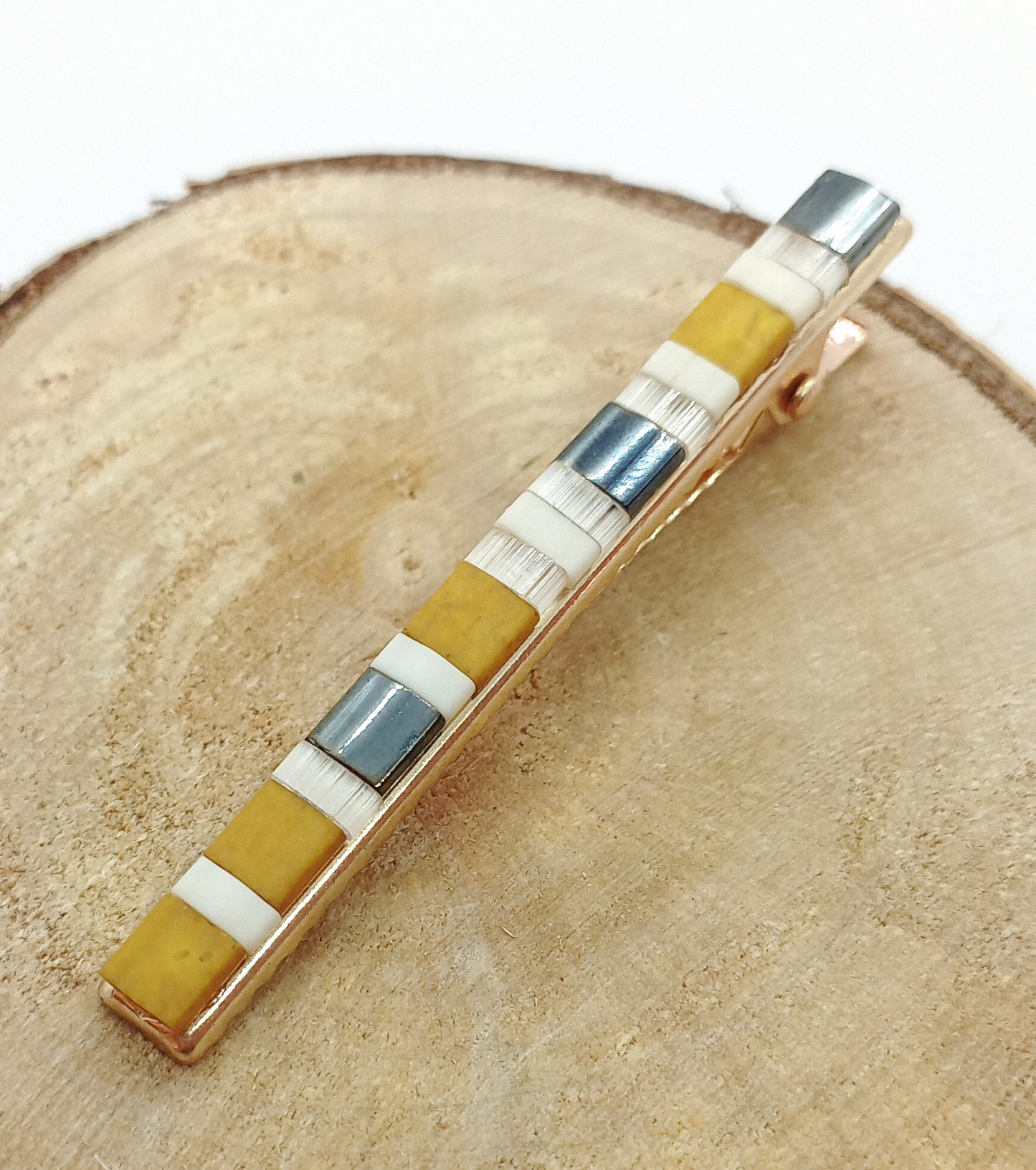 Barrette en métal doré et en perles de couleurs posé sur un rond de bois et un fond blanc.
