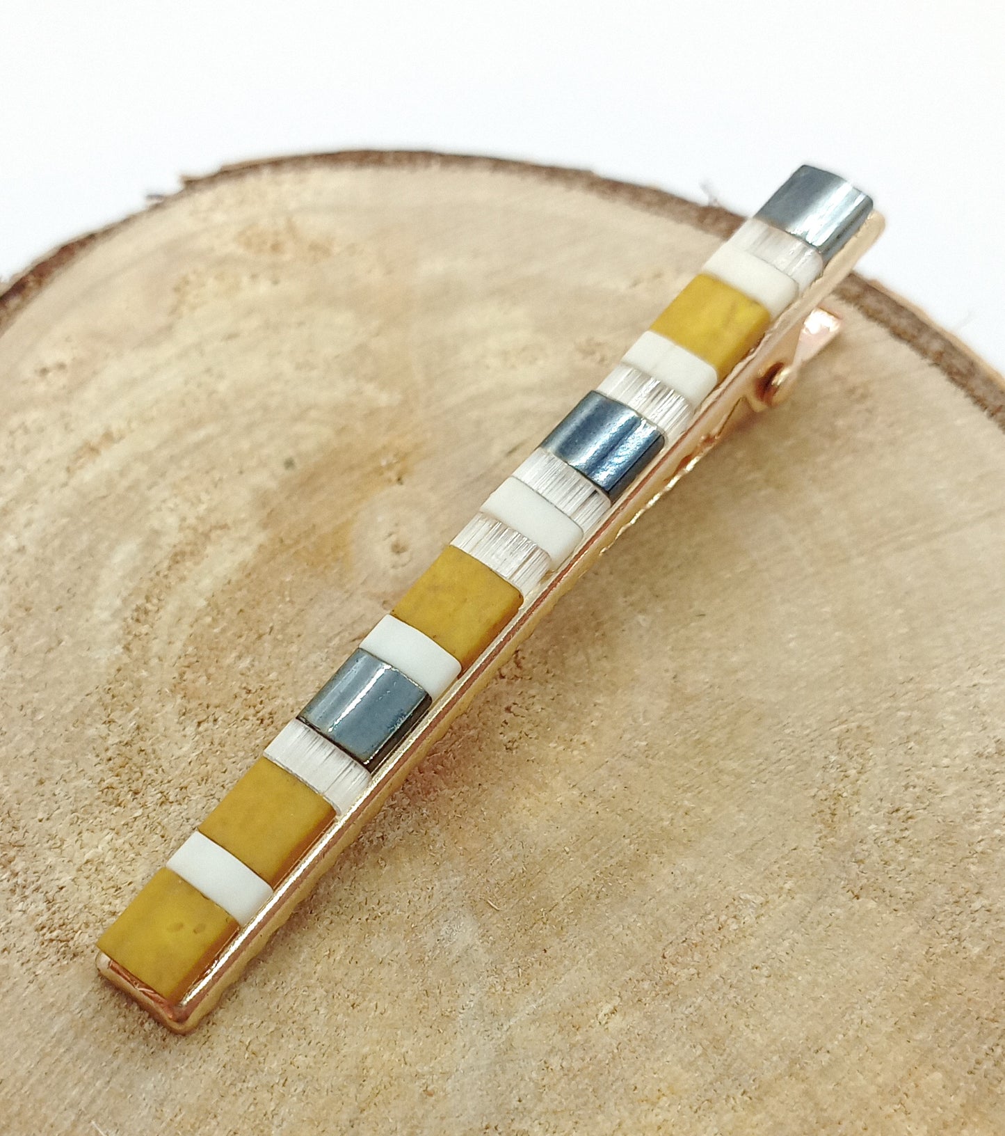Barrette en métal doré et en perles de couleurs posé sur un rond de bois et un fond blanc. 