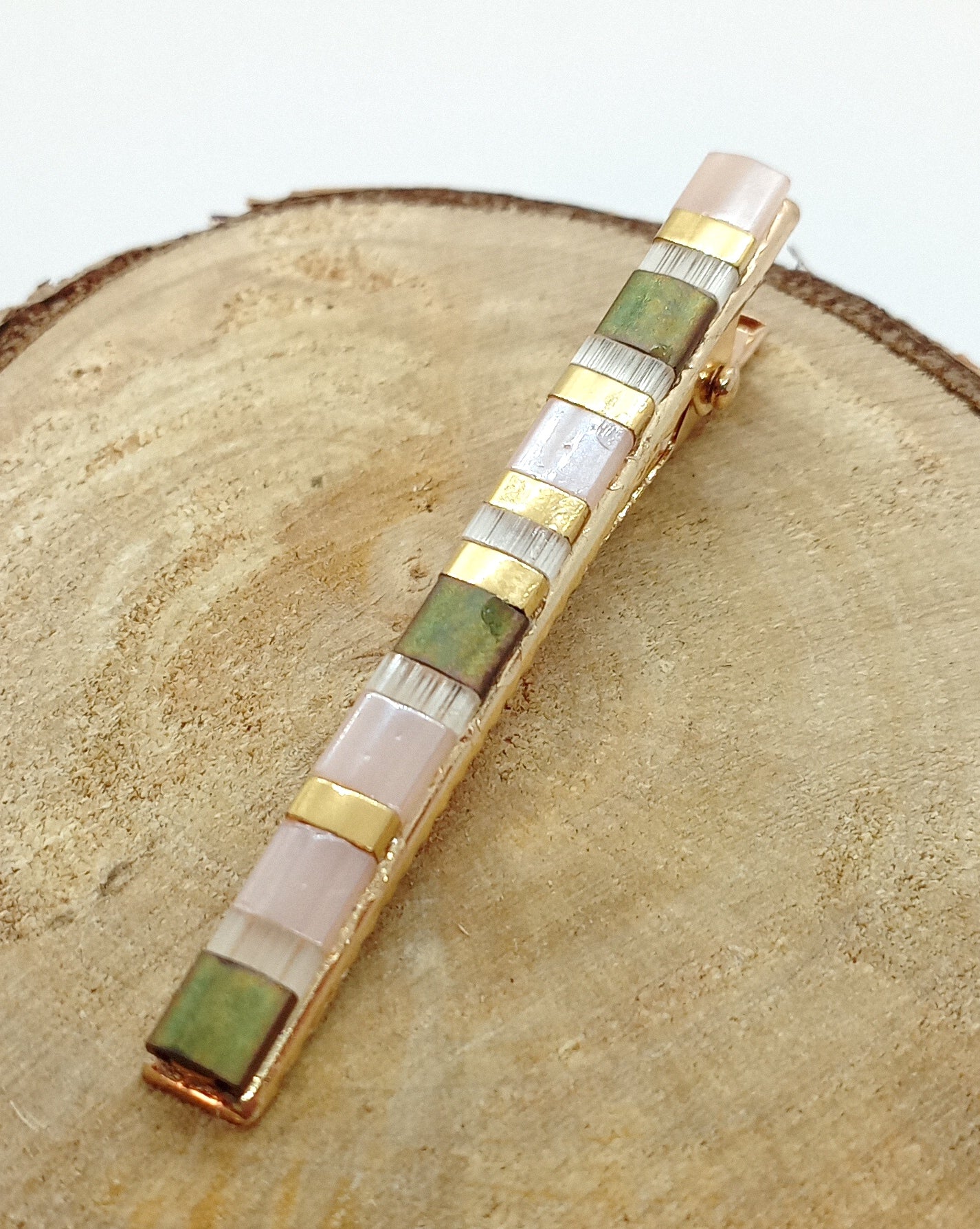 Barrette en métal doré et en perles miyuki tila posé sur un rond de bois et un fond blanc.