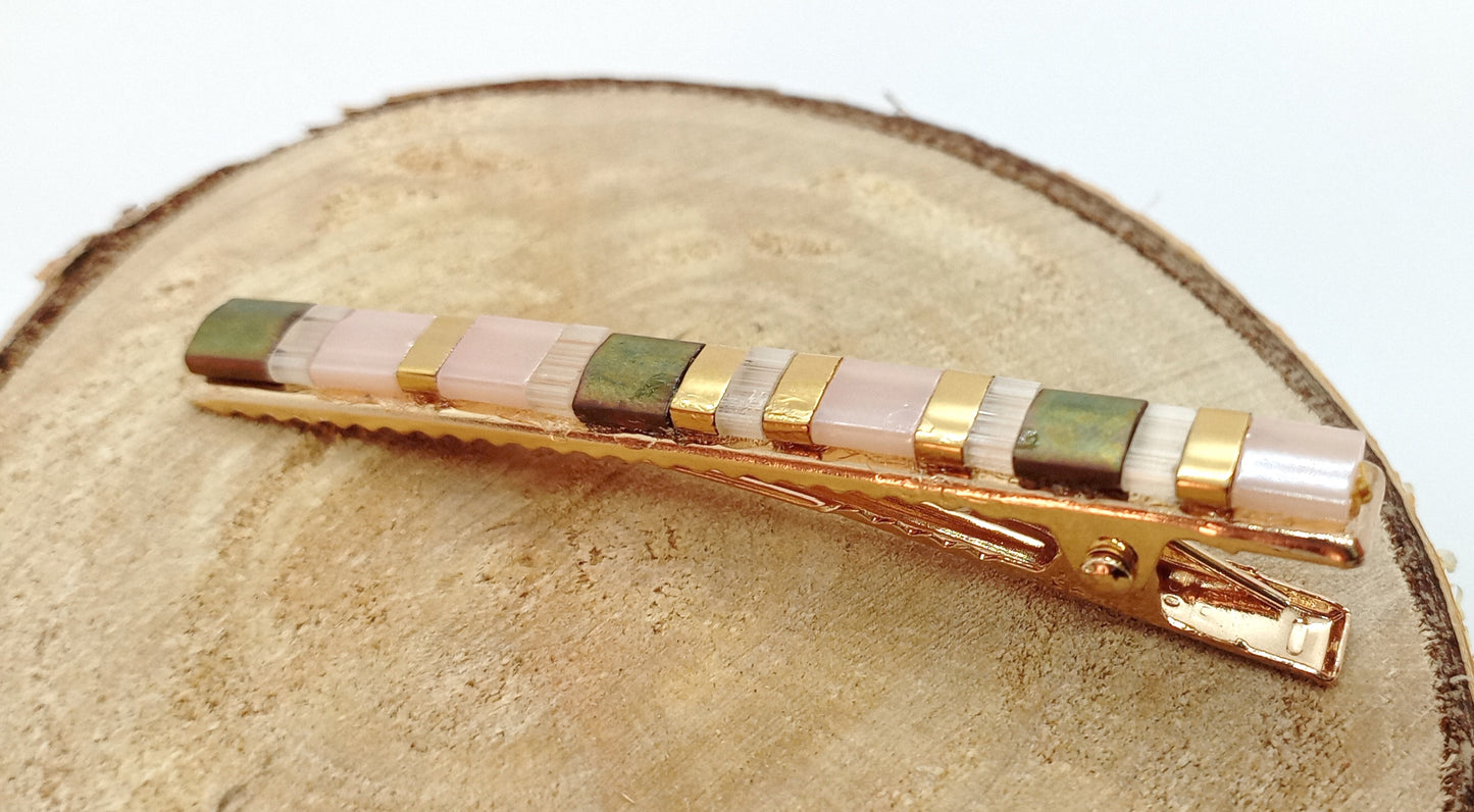 Barrette pour cheveux en métal doré et perles miyuki tila, posée sur un rond de bois et un fond blanc.
