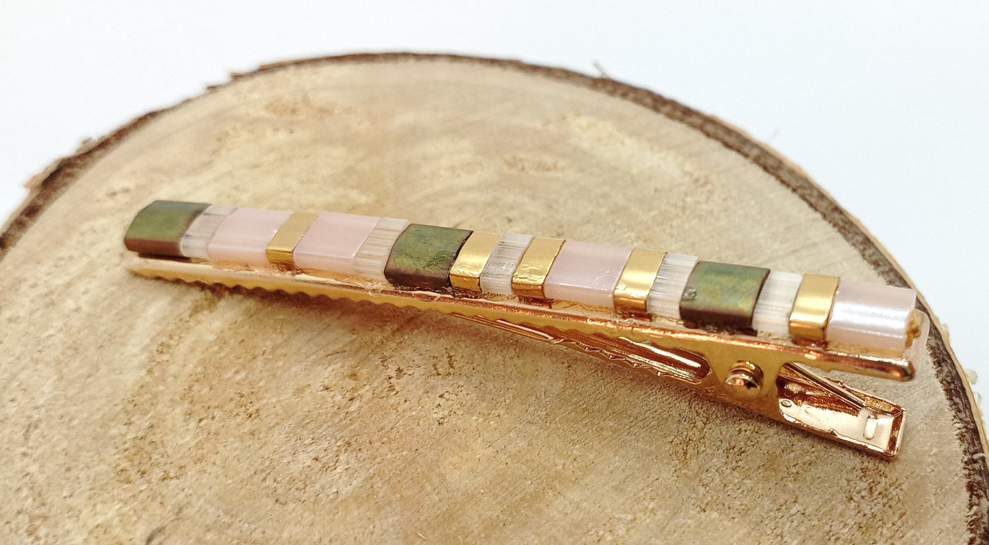 Barrette pour cheveux en métal doré et perles miyuki tila, posée sur un rond de bois et un fond blanc. 