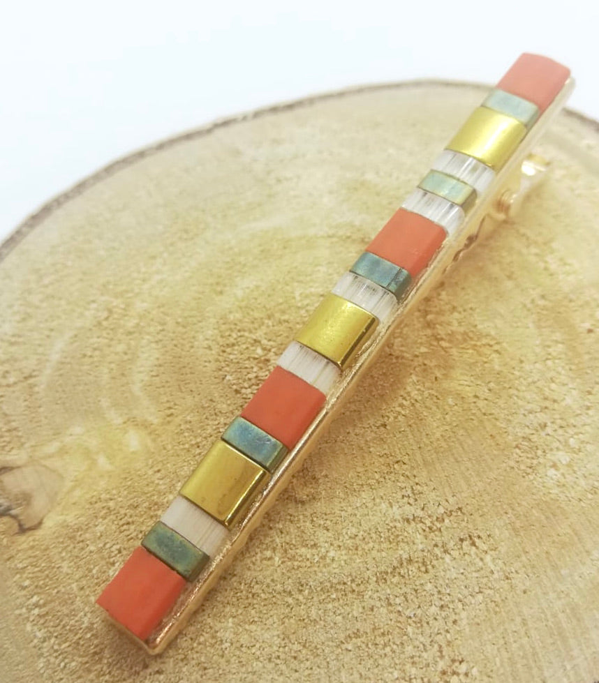 Barrette pour cheveux type pince crocodile en métal doré et perles miyuki tila, posée sur un rond de bois.