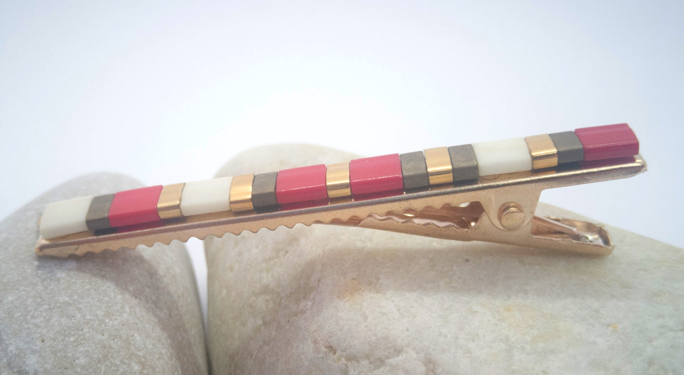 Barrette pour cheveux type pince crocodile en métal doré et perles miyuki tila, posé sur des cailloux et un fond blanc.