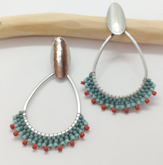 Boucles d'oreilles en acier avec tissage de perles miyuki bleu et orange, posées sur une branche et un fond blanc