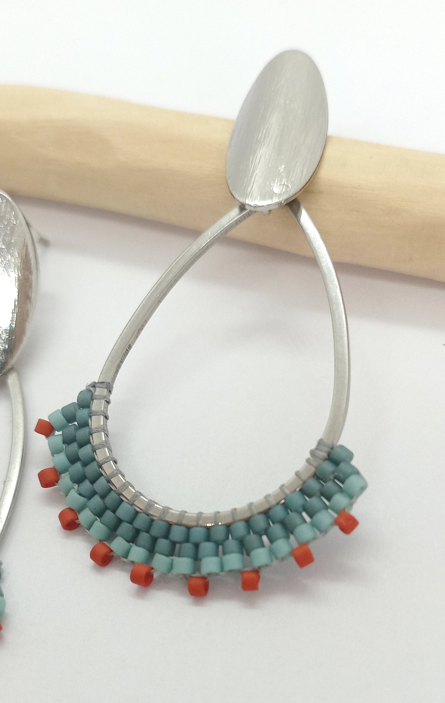 Boucles d'oreilles en forme de goutte en acier argenté et perles miyuki tissées bleues, sur une branche de bois et un fond blanc.
