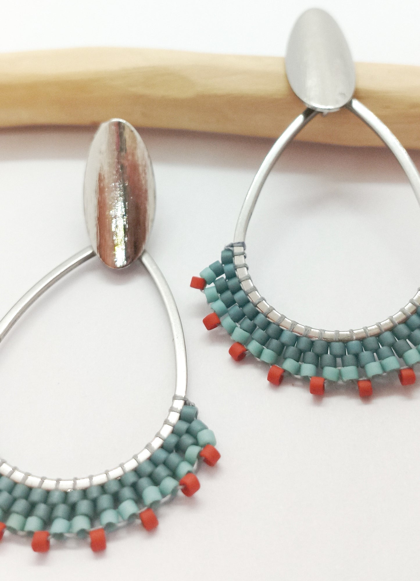 Boucles d'oreilles en forme de goutte en acier argenté et en tissage de perles miyuki, sur un fond blanc.