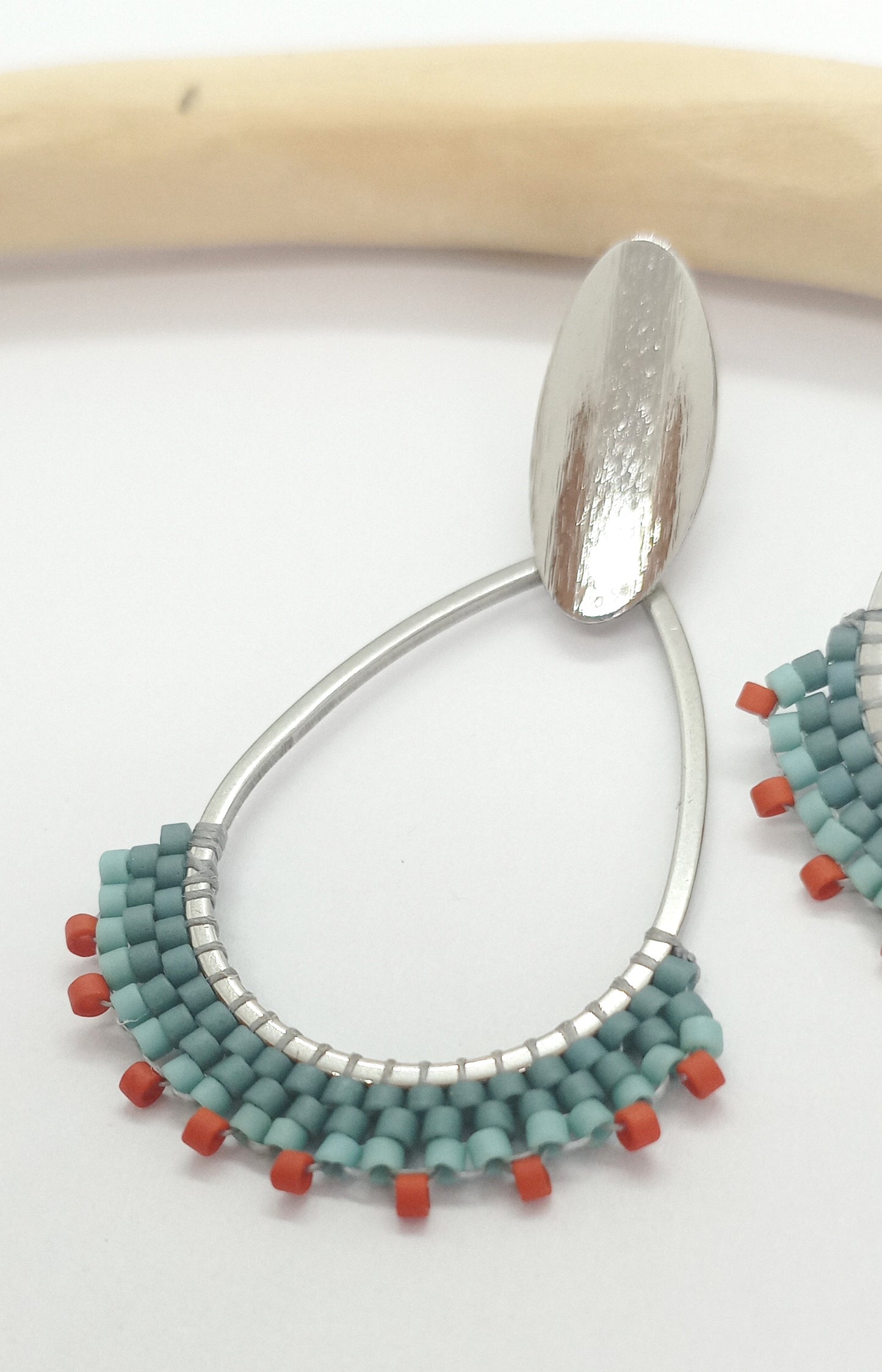 Boucles d'oreilles en acier argenté et tissage de perles miyuki posées sur un fond blanc.