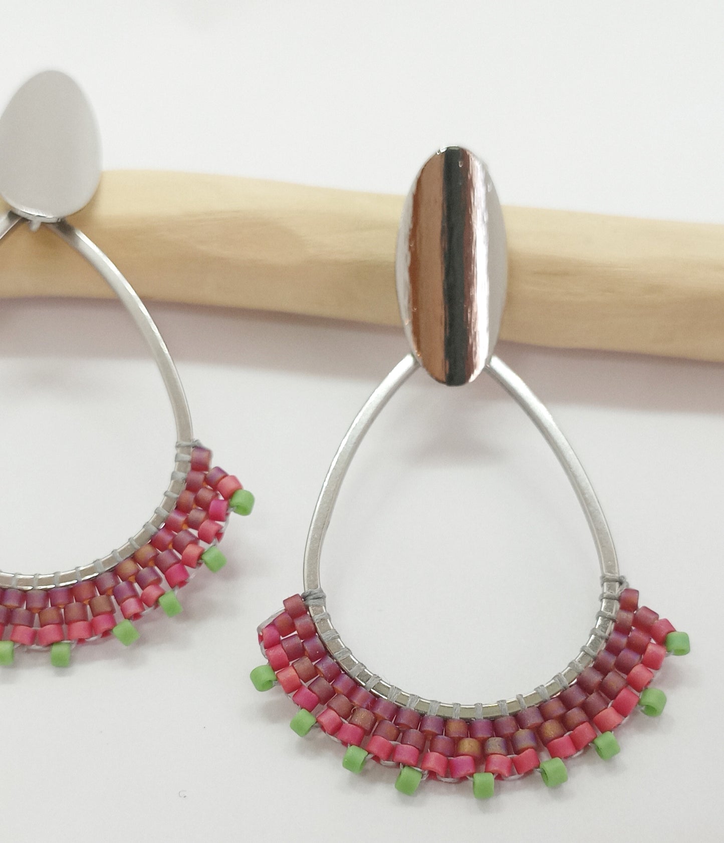 Boucles d'oreilles en acier argenté et perles miyuki tissées, posées sur une branche et un fond blanc.