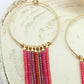 Créoles en laiton doré et perles miyuki rouge et rose pendantes, posées sur un rond de bois