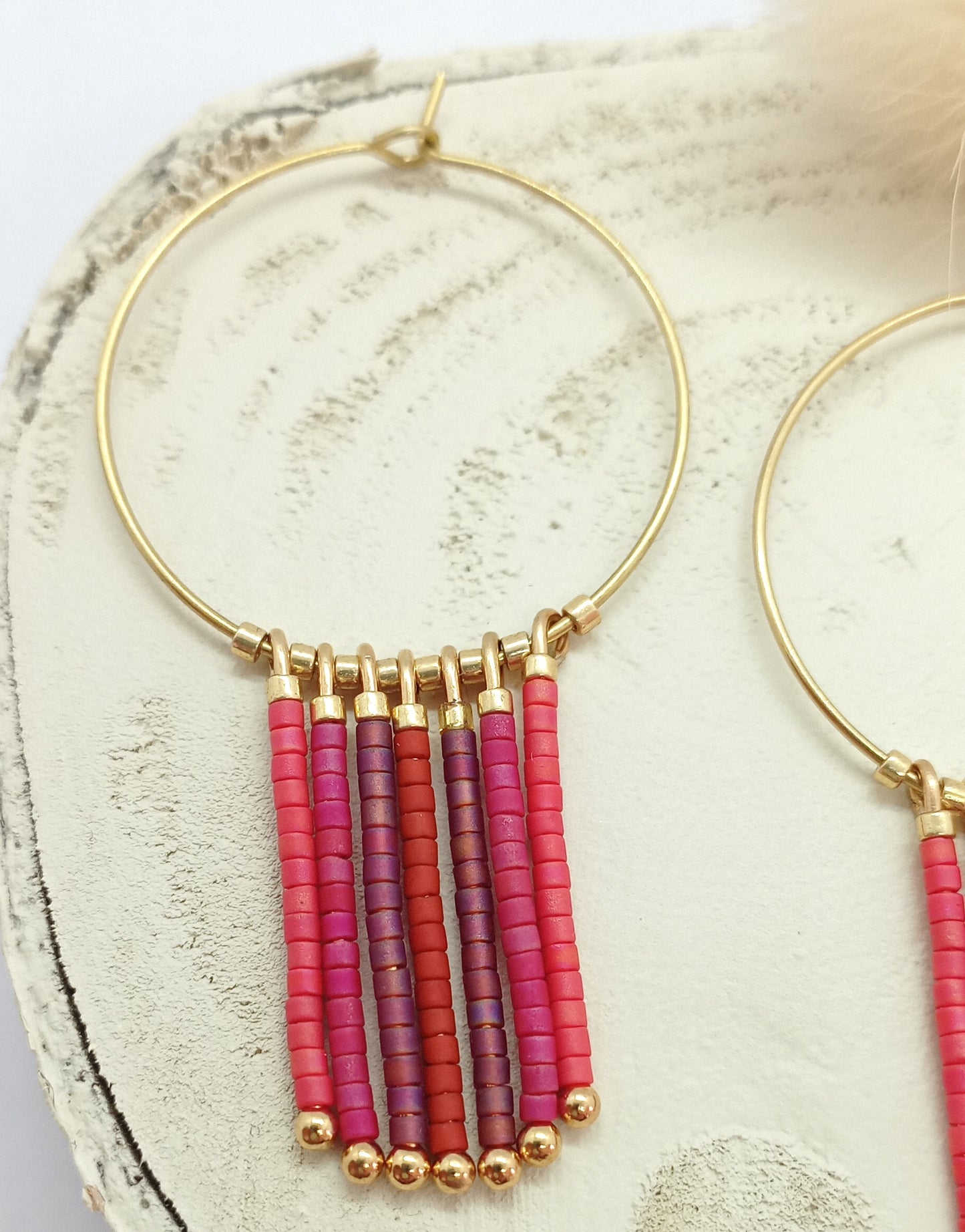 Créoles en laiton doré et perles miyuki rouge et rose pendantes, posées sur un rond de bois