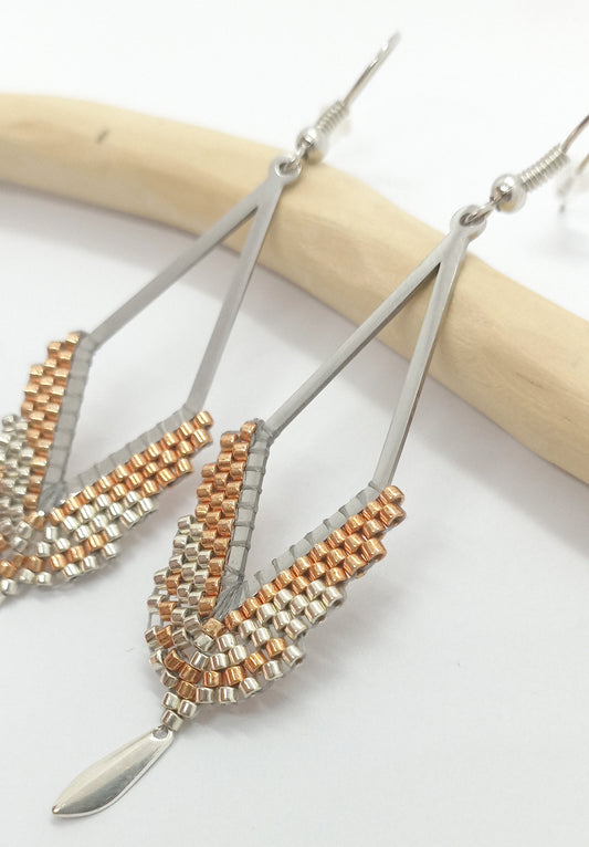 Boucles d'oreilles en forme de losange en acier argenté et perles miyuki tissées, posée sur une branche de bois clair