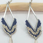 Boucles d'oreilles en forme de losange ajouré et en perles miyuki tissées bleu marine sur un fond blanc et bois clair