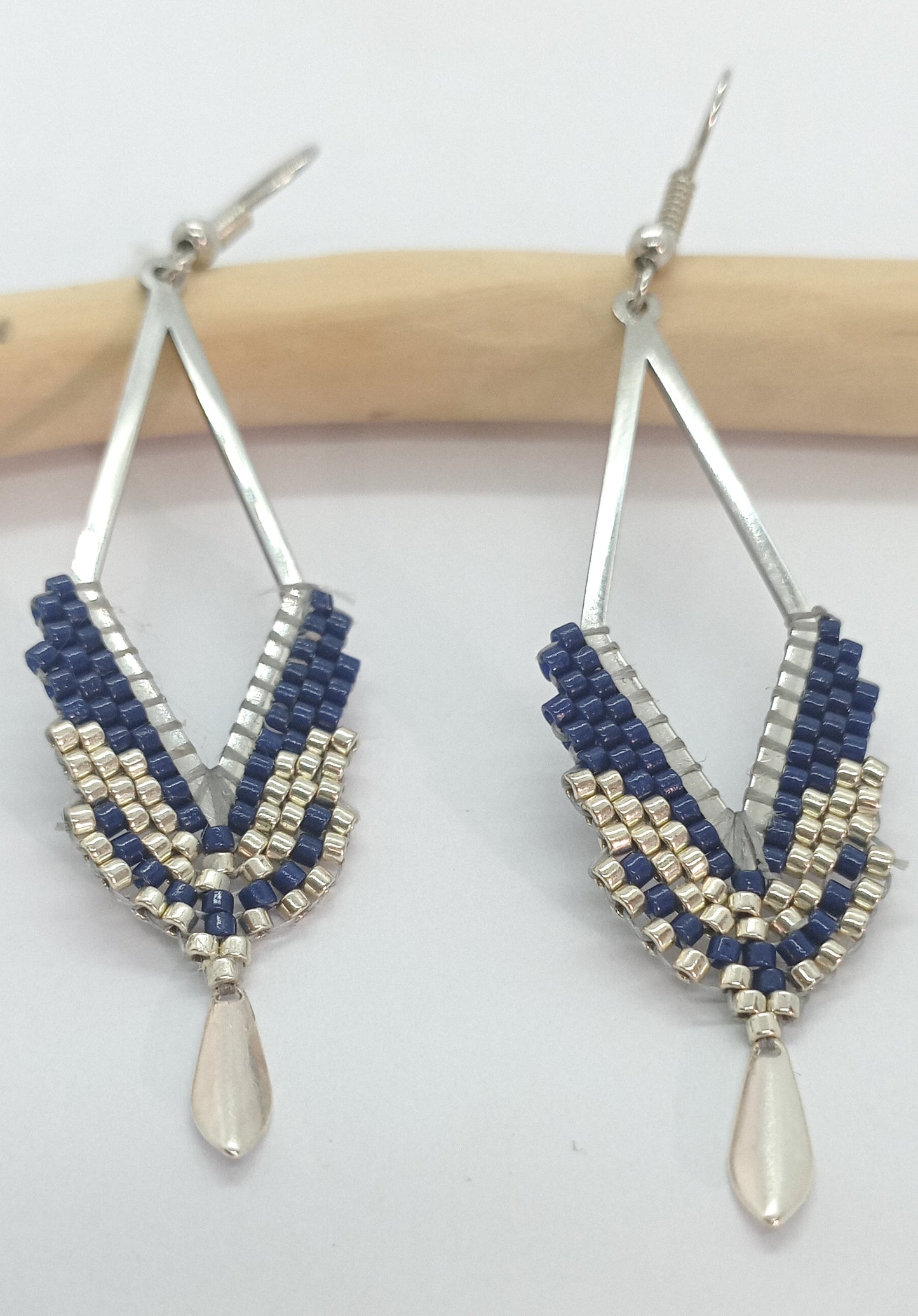 Boucles d'oreilles en forme de losange ajouré et en perles miyuki tissées bleu marine sur un fond blanc et bois clair