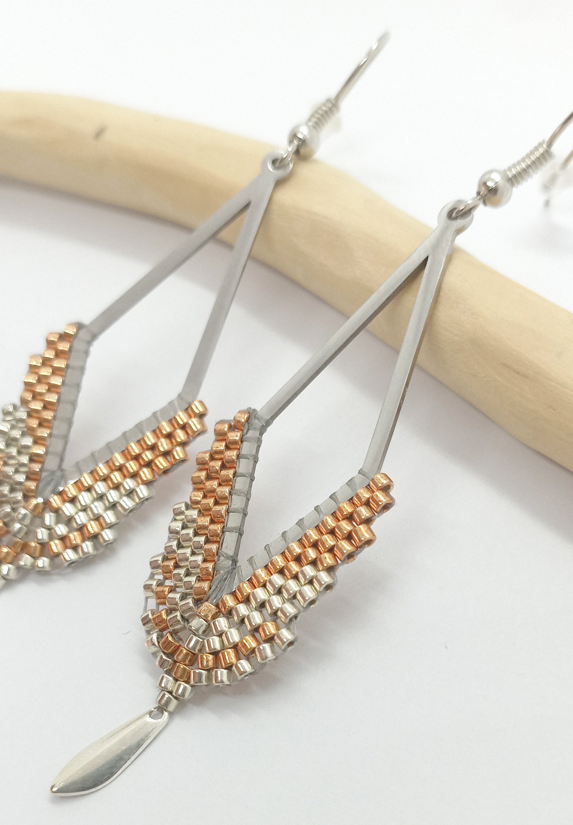 Boucles d'oreilles en forme de losange en acier argenté et perles miyuki tissées, posée sur une branche de bois clair 