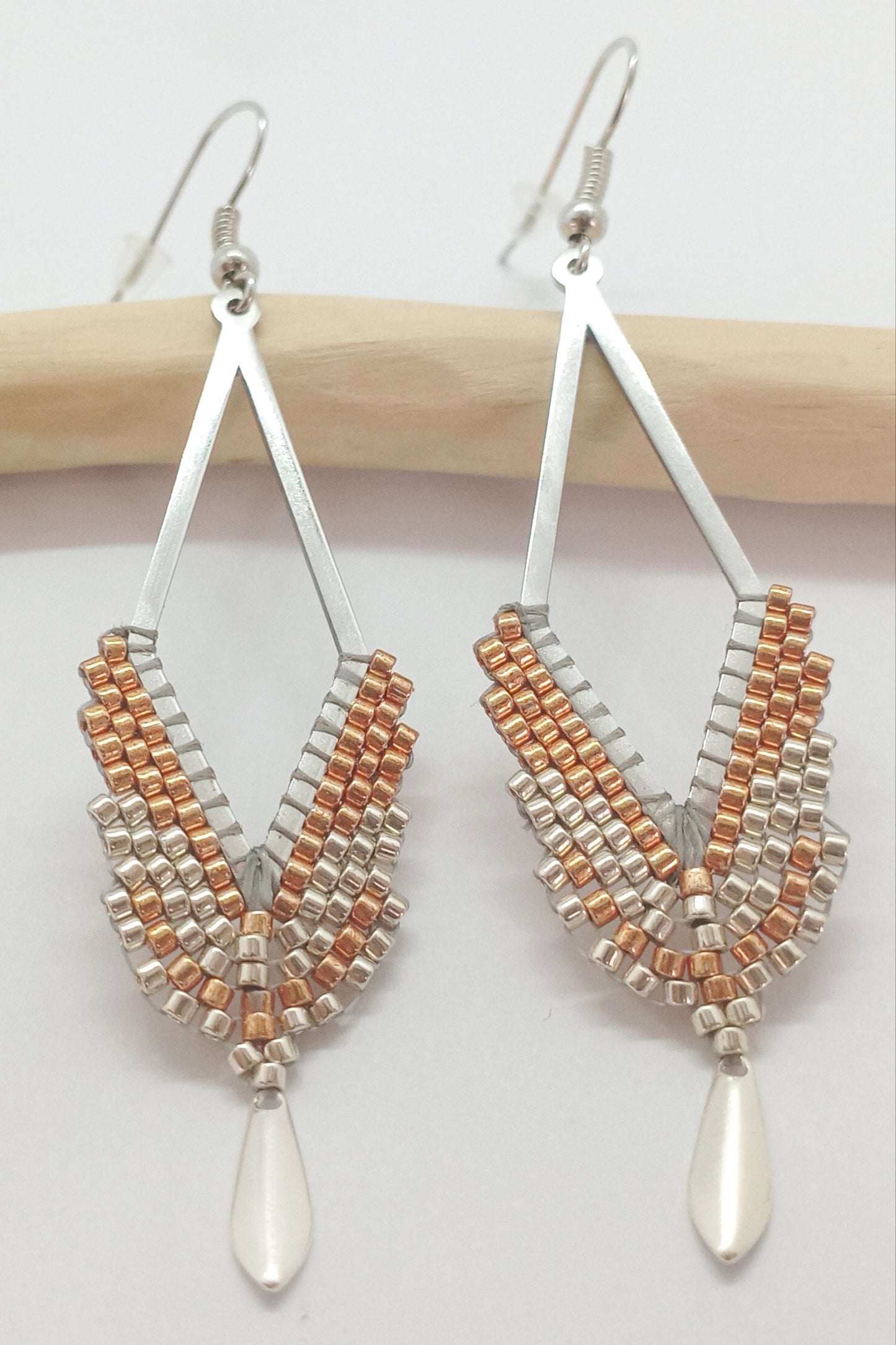 Boucles d'oreilles en forme de losange ajouré en acier argenté et perles miyuki tissées avec sequin argenté, posées sur une branche de bois clair 