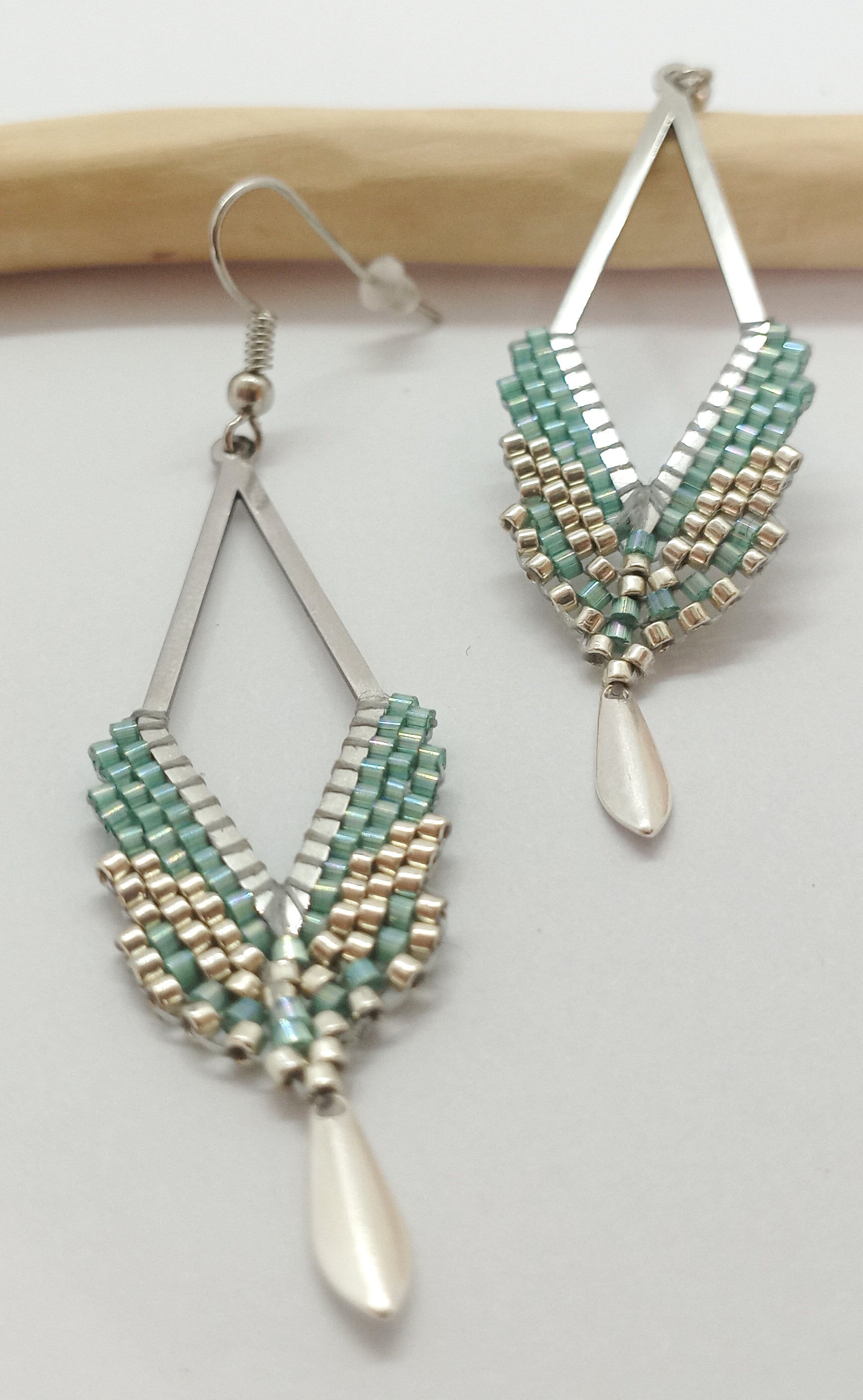 Boucles d'oreilles en fore de losange en acier argenté et perles miyuki tissées  avec  sequin argenté. Posées sur fond blanc et bois clair. 